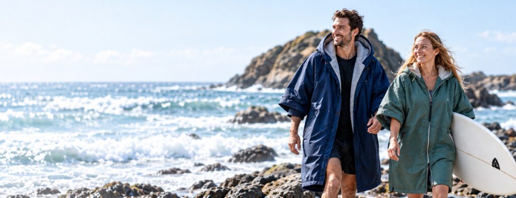 Illustrative adult models wearing navy and sage changing robes on a rocky coastline