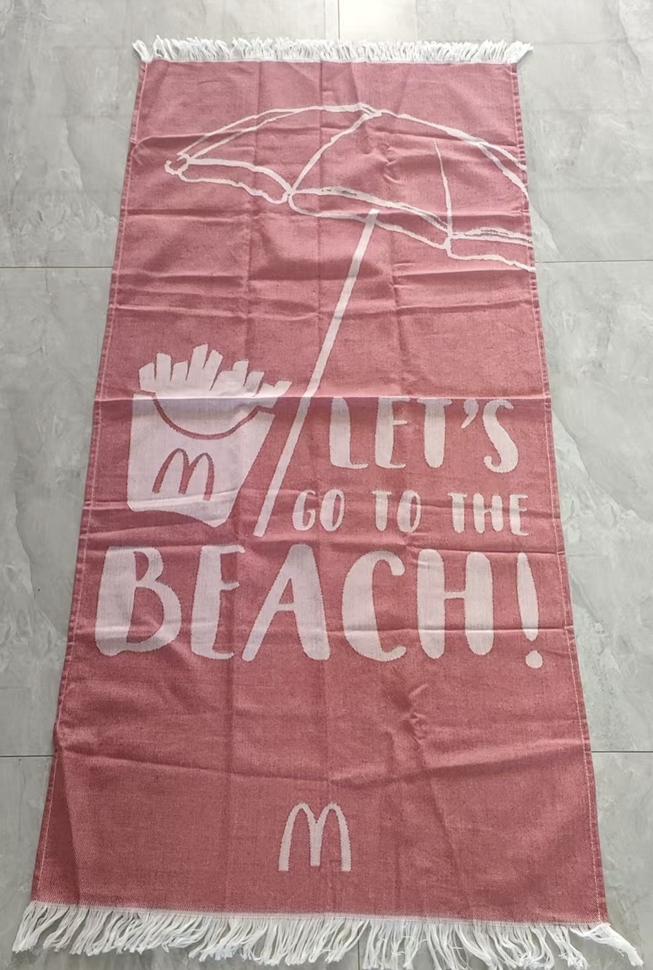 Pink fringed beach towel with a woven umbrella and beach design