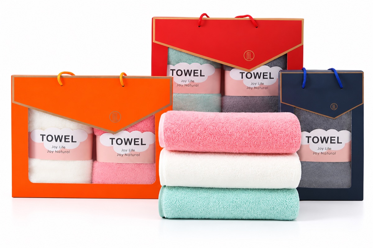 Towel gift boxes with folded towels in orange, red, and navy packaging on a white background