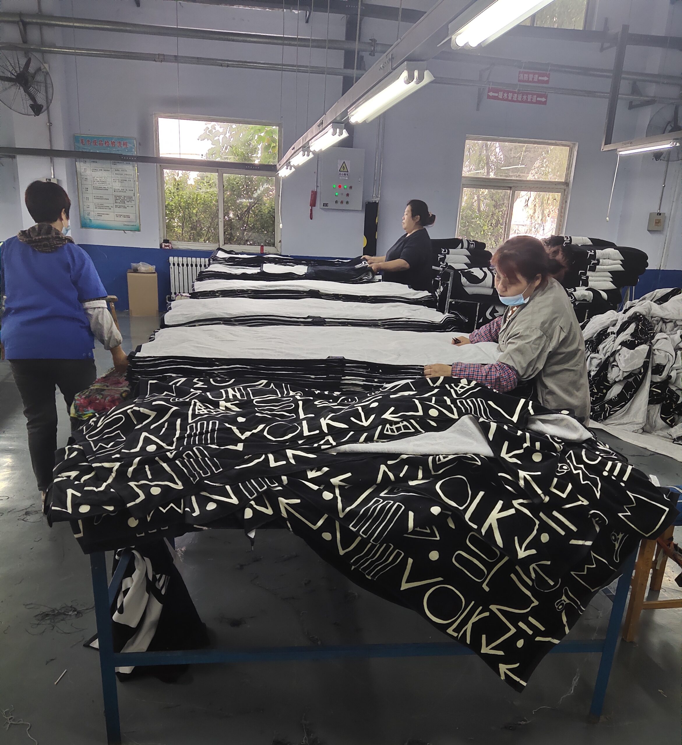 Factory workers inspecting and folding black-and-white printed cotton beach towels